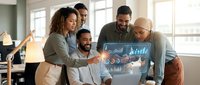Diverse business team collaborating around laptop displaying financial charts and data analytics in modern office environment with natural lighting.