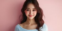 Young Asian woman with long dark wavy hair and natural makeup smiling warmly at camera while wearing light blue sweater against pink background. Professional portrait.