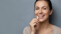 Young woman with dark hair and fair complexion brushing teeth with toothbrush against neutral gray background. Dental hygiene and oral care concept.