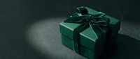 Elegant dark green gift box with velvet ribbon bow on moody dark background, luxury holiday present for Christmas or special occasion.