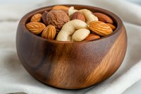 Mixed nuts in wooden bowl including almonds walnuts cashews and hazelnuts for healthy snacking and cooking ingredients on white fabric background.
