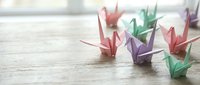 Colorful paper origami cranes arranged on wooden surface with soft natural lighting. Traditional Japanese folding art craft for meditation, decoration, and creative projects.