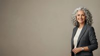 Mature woman with gray curly hair wearing dark blazer and white shirt standing against neutral background, suitable for corporate, business, and professional portraits.