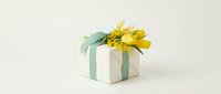 White gift box with mint green ribbon and yellow flower decoration on neutral background for celebrations and special occasions.