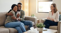 Happy African American couple embracing on couch during therapy session with professional counselor in modern office setting for relationship support.