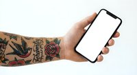 Tattooed hand holding smartphone with blank white screen mockup for app presentation and digital design projects.