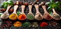 Aromatic spices and herbs in wooden spoons on dark rustic background with fresh basil leaves, star anise and peppercorns. Culinary seasoning concept.