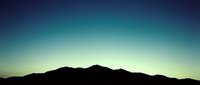 Silhouetted mountain range against a serene gradient sky transitioning from deep blue to soft yellow at horizon, evoking dawn or dusk atmosphere for nature and landscape design projects.