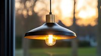 Vintage pendant lamp with glowing Edison bulb against blurred sunset background creates warm atmospheric lighting for modern interior design and decor.