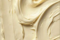 Creamy vanilla frosting texture with smooth swirls and ripples creating an abstract pattern background, close-up macro photography showing rich buttery surface detail.