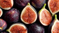 Fresh ripe purple figs cut in half showing juicy pink flesh and seeds on dark background, organic seasonal fruit composition for healthy eating.