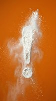 White flour exclamation mark exploding with powder dust on vibrant orange background for baking and cooking concepts.