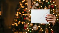 Woman holding blank white card with festive holiday lights and decorated tree in soft focus background. Seasonal greeting card mockup for winter celebrations and promotional messaging.