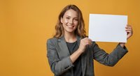 Young professional businesswoman holding blank white paper sign with copy space for text on vibrant orange background for marketing presentations.