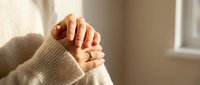 Woman hands in cozy beige sweater clasped together in warm sunlight by window. Comfort, relaxation, mindfulness, self-care concept for wellness content.