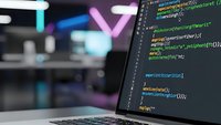 Software developer coding on laptop screen with colorful syntax highlighting in modern office environment for programming projects and web development.