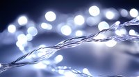 Glowing white LED string lights creating magical bokeh effect against dark background, decorative lighting for holidays and celebrations.