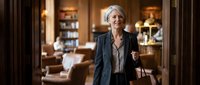 Confident senior businesswoman with gray hair standing in elegant hotel lobby wearing professional dark suit, corporate executive portrait for business presentations.