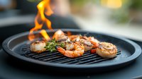 Grilled jumbo shrimp and scallops with fresh herbs on black cast iron pan, flames visible in background creating dramatic culinary atmosphere.