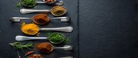 Colorful spices and herbs arranged on vintage spoons against dark slate background for culinary cooking and seasoning recipes.