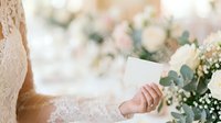 Bride in lace wedding dress holding blank white card with eucalyptus and baby's breath flowers, suitable for invitations, announcements, and wedding stationery designs.