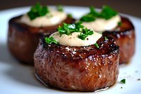 Juicy grilled beef tenderloin medallions topped with herb butter and fresh parsley garnish on white plate, close-up view showing mouthwatering seared texture.