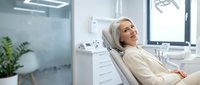 Relaxed middle-aged Caucasian woman patient sitting comfortably in modern dental office chair during routine checkup visit.