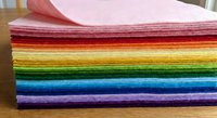 Stack of colorful rainbow felt fabric sheets arranged in gradient order from pink to purple on wooden surface for crafting and sewing projects.