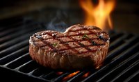 Juicy beef steak with grill marks cooking on barbecue with flames in background, perfect for food advertising and menu design.