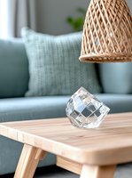 Modern living room interior with crystal glass decoration on wooden coffee table, rattan pendant lamp and sage green sofa with textured cushion in background.