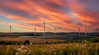 Wind turbines generating renewable energy in rural landscape at dramatic sunset with golden orange clouds and rolling hills for sustainable power concepts.