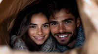 Young diverse couple in warm winter sweaters sharing intimate moment with genuine smiles, close-up portrait against blurred background.