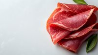 Fresh sliced prosciutto ham with green bay leaves arranged on white background, macro food photography showing meat texture and marbling pattern.
