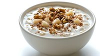 Creamy yogurt bowl topped with diced pears, crunchy granola, and nuts in white ceramic bowl against bright background, healthy breakfast concept.