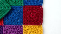 Colorful crocheted granny squares in bright rainbow colors including green, blue, red, purple and yellow arranged on white background for crafting projects.