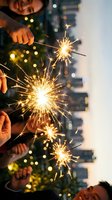Hands holding lit sparklers against urban cityscape with bokeh lights and festive atmosphere for celebrations and New Year events.