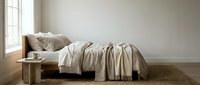 Minimalist bedroom interior with unmade bed, neutral bedding, wooden nightstand, and natural light from window for home decor design.