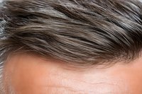 Close-up view of gray and brown hair strands showing natural texture and wave pattern against light skin, demonstrating aging process and hair care concept.