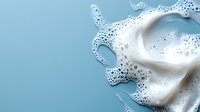 Fresh white milk splash with dynamic bubbles and foam creating organic flowing shapes on clean blue background for dairy advertising and beverage marketing.