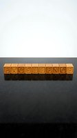 Wooden letter blocks spelling EXCELLENCE on a reflective dark surface, symbolizing quality, achievement, and high standards in business and education.
