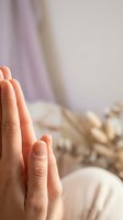 Hands pressed together in prayer position during morning meditation and mindfulness practice in serene bedroom setting with soft natural lighting.