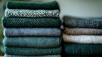 Stack of cozy knitted sweaters and cardigans in green, gray and beige tones folded neatly, showcasing winter fashion and warm clothing textures for seasonal wear.