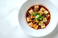 Spicy mapo tofu with minced meat and green onions in savory sauce served in white bowl on marble background, traditional Chinese Sichuan cuisine.