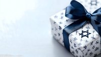 White gift box wrapped in star of David pattern paper with navy blue satin ribbon bow against light background, festive Hanukkah celebration concept.