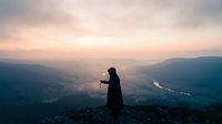 Silhouette of person standing on mountain peak at sunrise with misty valley landscape and dramatic sky for meditation and inspiration concepts.