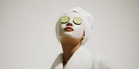 Young woman in white bathrobe with cucumber slices on eyes enjoying spa treatment for skincare and relaxation at home wellness routine.