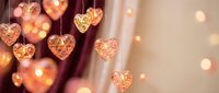 Romantic golden heart-shaped decorations hanging with warm bokeh lights creating cozy atmosphere for Valentine's Day celebration and love themes.