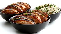 Grilled teriyaki chicken breast sliced and served in black ceramic bowls with steamed rice garnished with fresh herbs, photographed on white background.