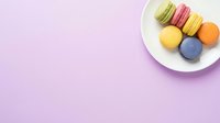 Colorful macarons arranged on white plate against soft lavender background, overhead view with copy space for bakery, dessert, and confectionery design projects.