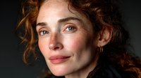Young redhead woman with curly hair and freckles smiling warmly at camera against dark background for portrait photography and lifestyle content.